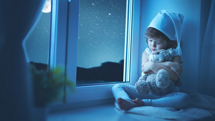 Little girl in a winter hat with a teddy bear at night