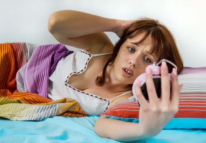 Woman looking at alarm clock in bed
