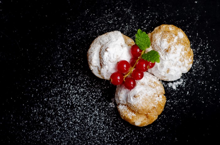 Three cream puffs with currants and mint on black background