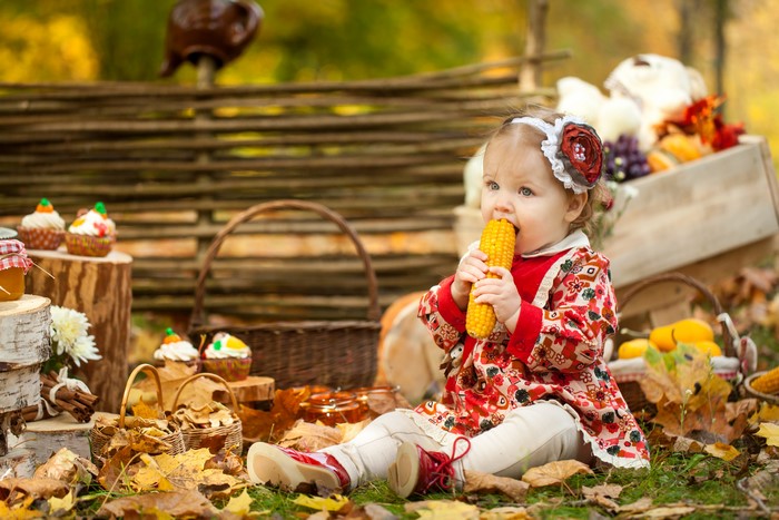 Little girl eating corn in autumn