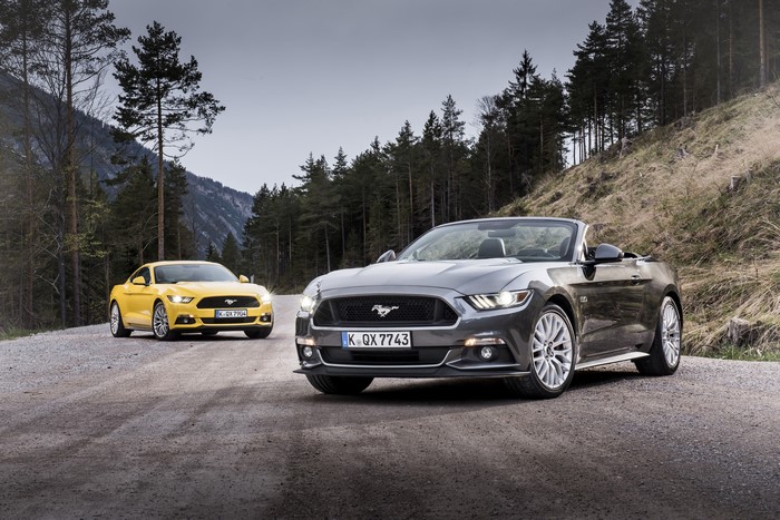 Two Ford Mustang cars on a mountain road