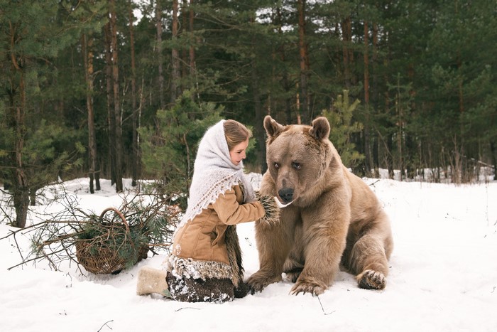 Girl and brown bear in snowy forest