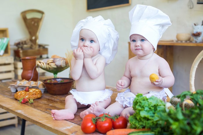 Two babies dressed as chefs with vegetables