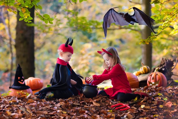 Children in Halloween costumes with pumpkins in autumn forest