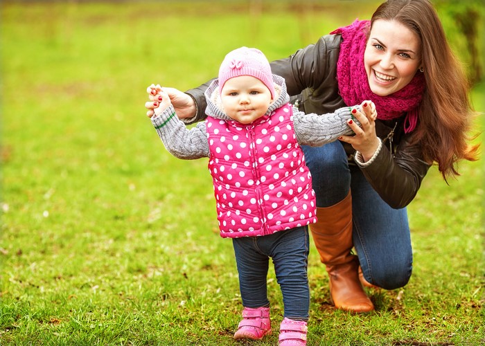 Mother helping baby walk on grass