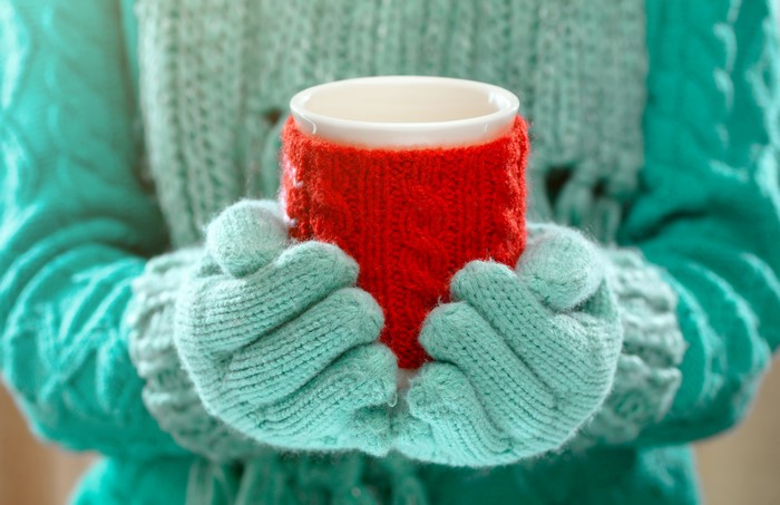Hands holding a mug with a red knitted sleeve