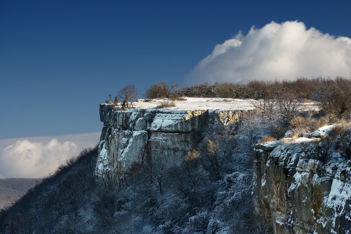 Snow-covered cliffs and trees under a blue sky