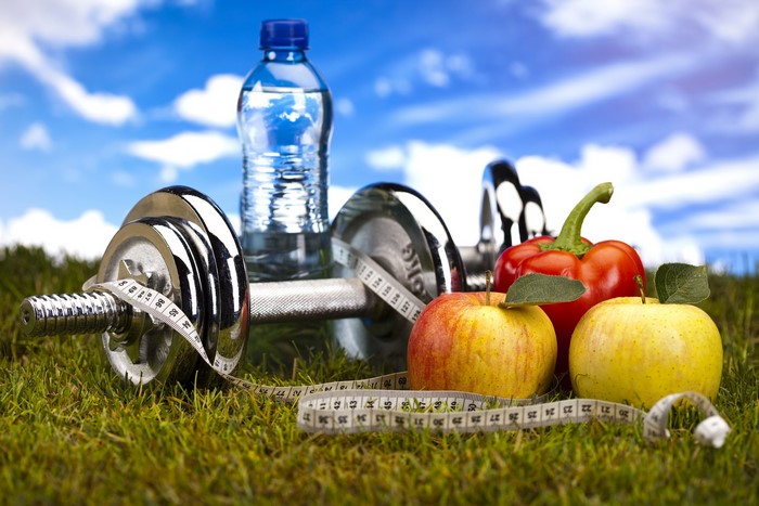 Dumbbells, water bottle, apples, and pepper on grass