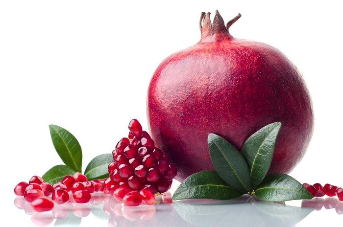 Pomegranate with seeds and leaves on white background
