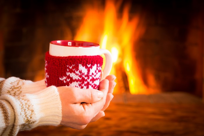 Hands holding a mug by a fireplace