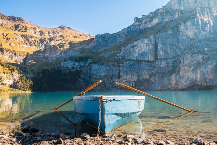 Blue rowboat with oars on a clear lake with mountains