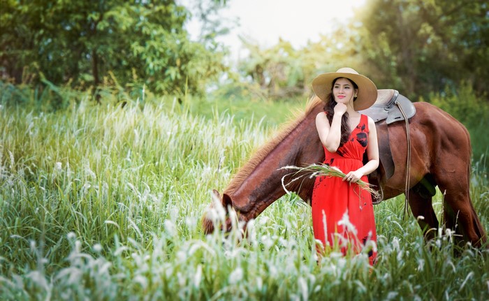 Asian Woman in Red Dress and Hat with Horse in Grass Field