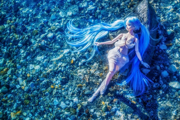 Doll with blue hair underwater on stones