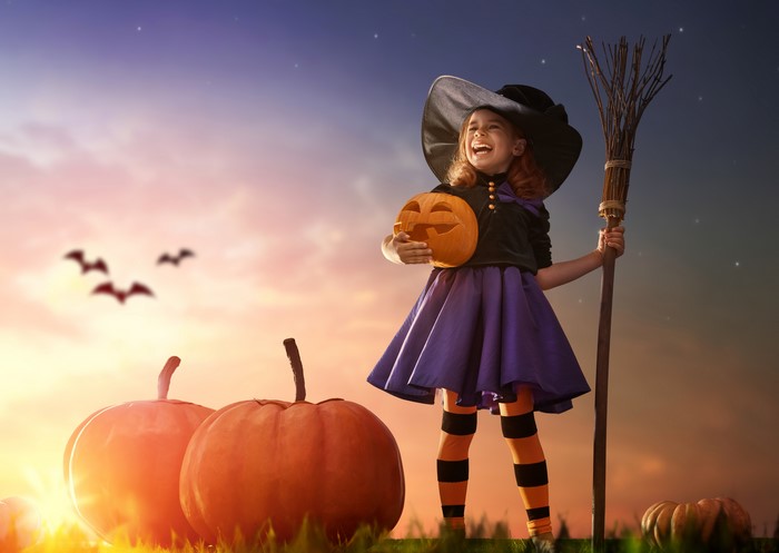 Little girl in witch costume with pumpkin and broom