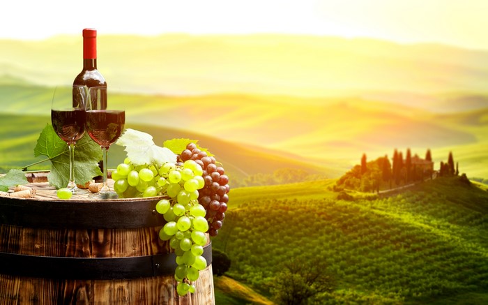 Wine bottle and glasses on barrel with grapes in Tuscany