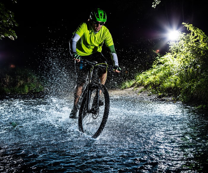 Man riding a bicycle through water at night
