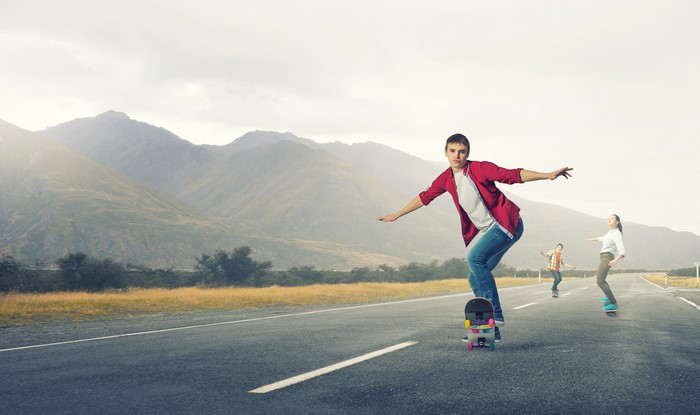 Three people skateboarding on a road with mountains