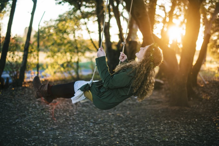 Girl on a swing in a forest at sunset