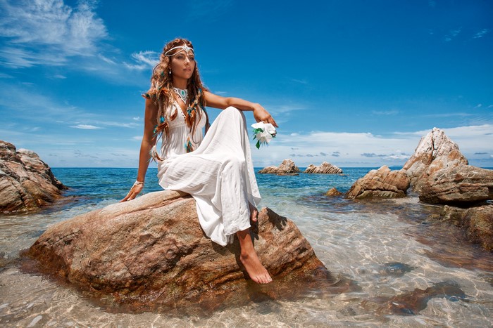 Woman in white dress sitting on a rock by the sea