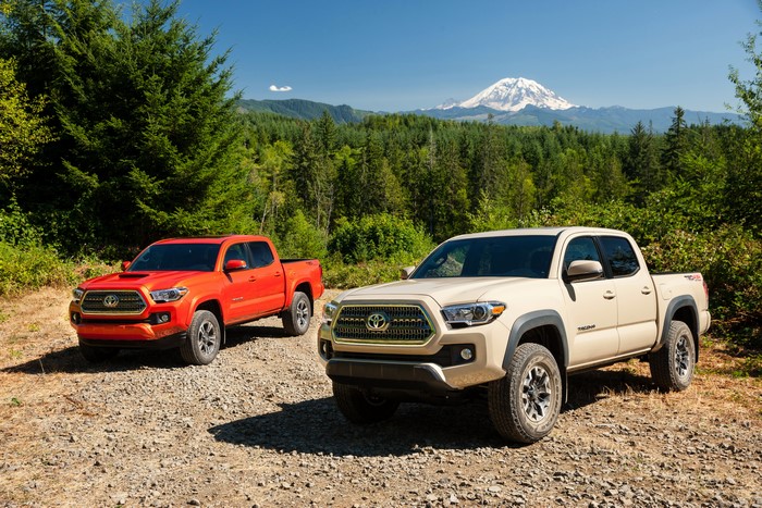 Two Toyota Tacoma TRD Sport trucks in a forest with a mountain