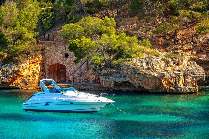 White yacht anchored in a turquoise bay near a stone boathouse