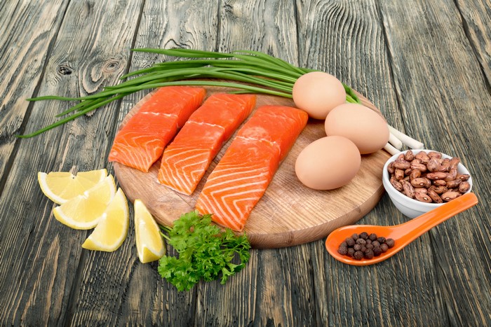 Salmon fillets, eggs, lemons, beans, and chives on a cutting board
