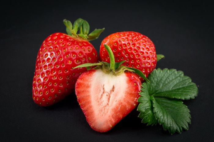 Three strawberries with leaves on black background