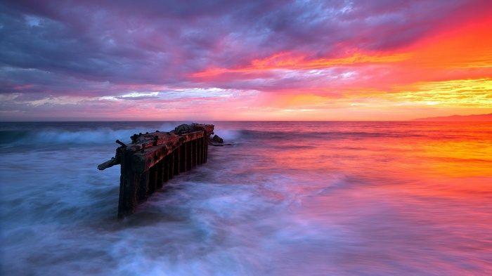 Ruined pier at sunset with colorful sky and ocean waves
