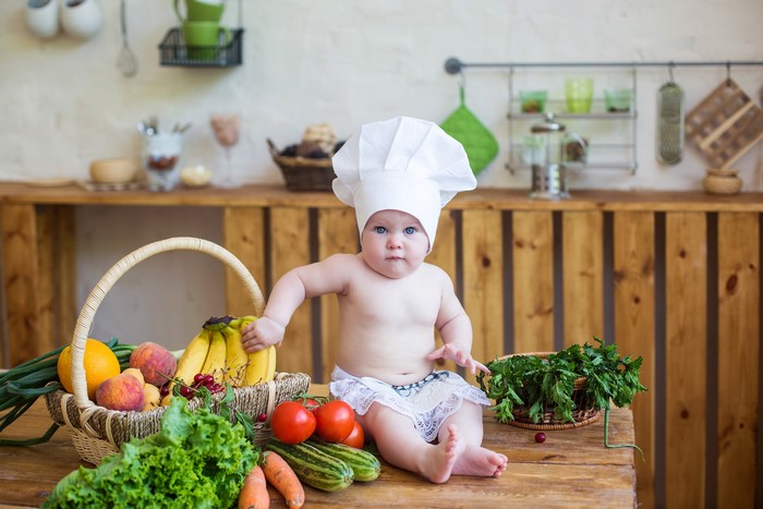 Baby in chef hat with fruits and vegetables