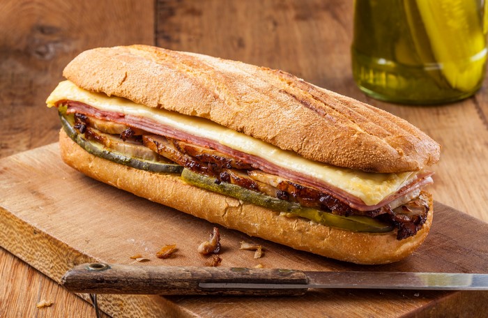 Sandwich with ham, cheese, and pickles on a cutting board