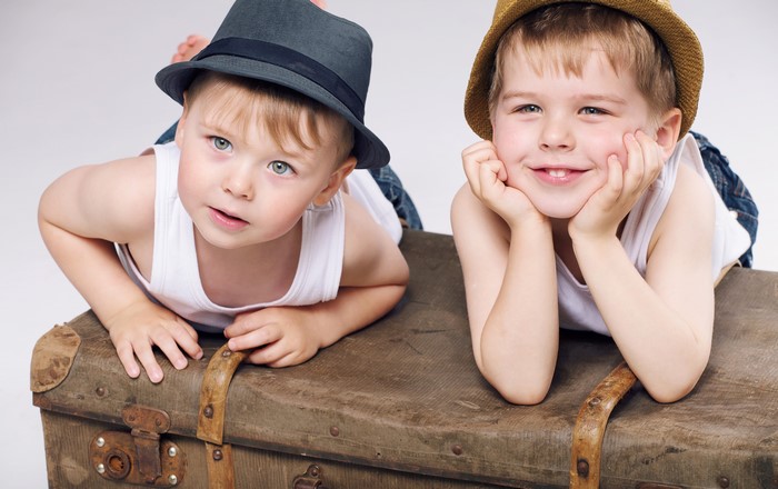 Two boys wearing hats on a suitcase