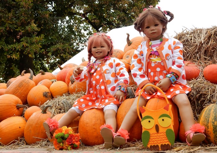 Two dolls dressed as little girls sitting among pumpkins