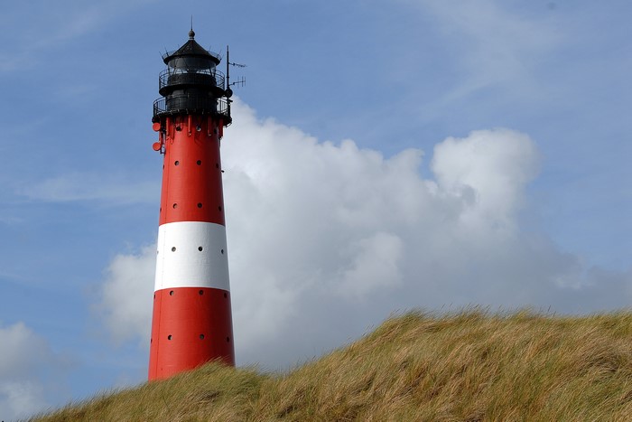 Red and white lighthouse on a grassy dune