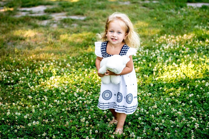 Little girl holding a teddy bear in a field of flowers