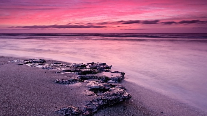 Pink sunset over a rocky beach with ocean waves