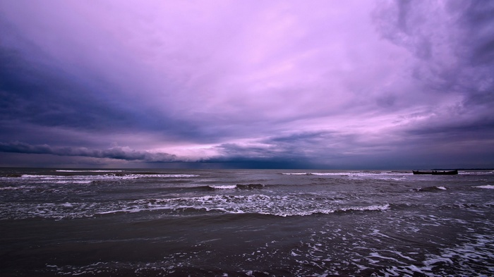 Stormy purple clouds over the ocean with a boat