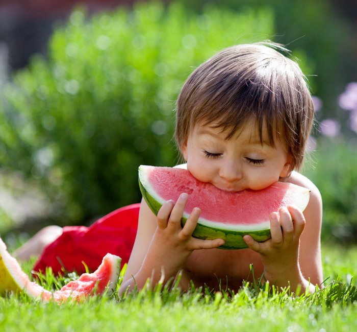 Boy eating a slice of watermelon on grass
