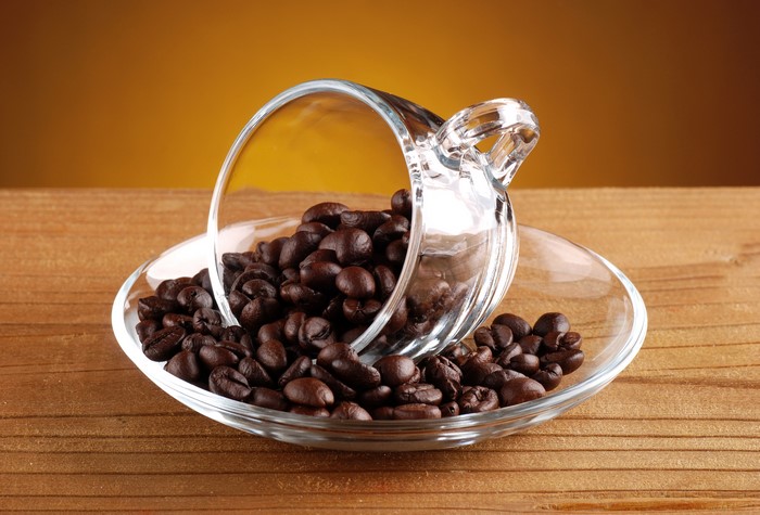 Coffee beans spilled from a glass cup onto a saucer