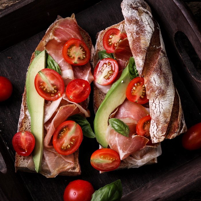Two open-faced sandwiches with ham, avocado, and tomatoes