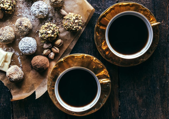 Two cups of coffee with assorted chocolates and nuts