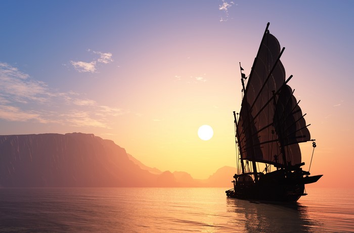 Junk ship sailing at sunset near mountains