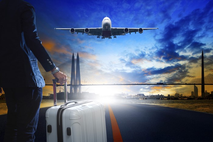 Man with suitcase watches airplane land over bridge at sunset
