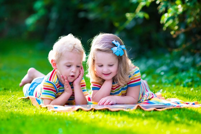 Two children reading a book on the grass