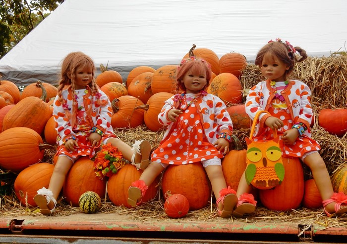 Three dolls dressed as little girls sitting on pumpkins