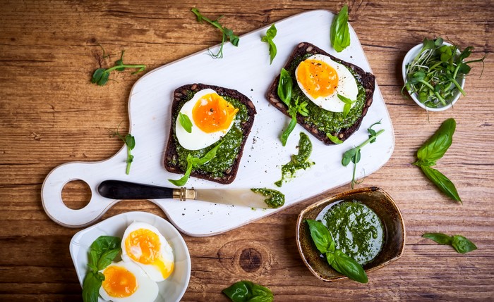 Two open-faced sandwiches with boiled eggs and pesto on a cutting board