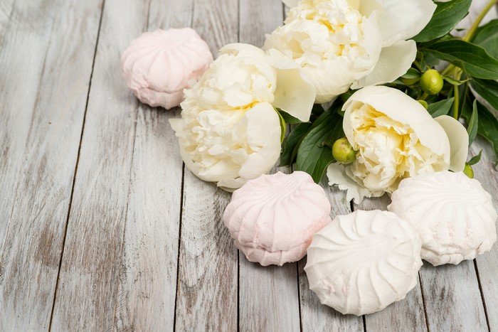White peonies and pink and white zefir on wooden planks