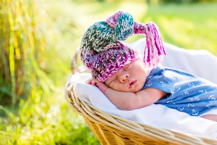 Baby sleeping in a basket wearing a knitted hat