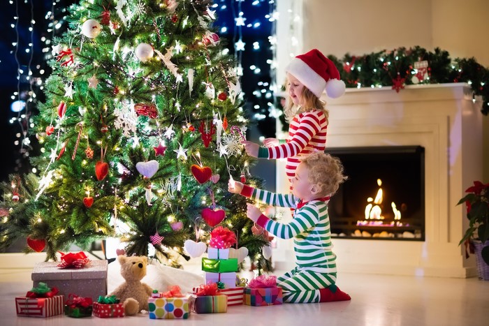 Children decorating a Christmas tree with gifts and fireplace