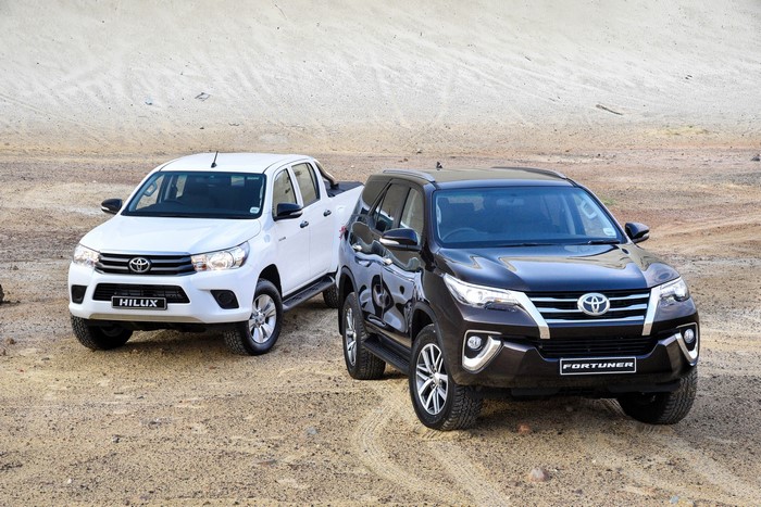 Two Toyota vehicles: a white Hilux and a dark Fortuner