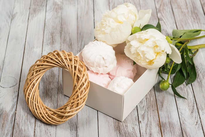 White peonies and sweets in a box on wood planks